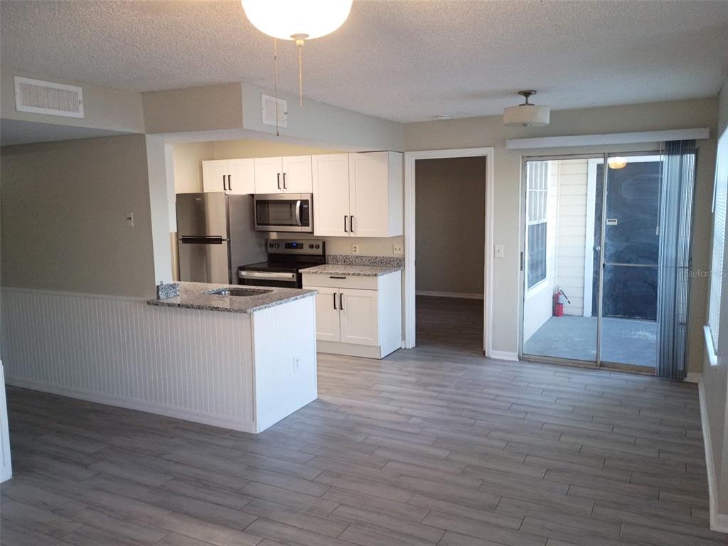 A kitchen with white cabinets and granite countertops opens into a living area with flooring — 1037 S HIAWASSEE ROAD UNIT 2818, ORLANDO, FL