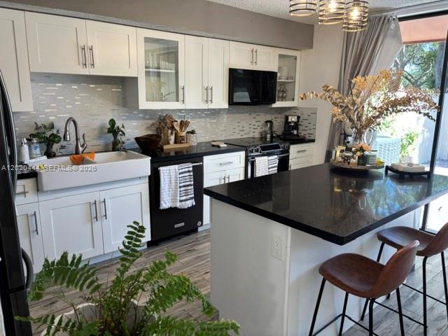 A white kitchen features a black island, dark countertops, and a farmhouse sink — 10621 SW 79th Ter, Miami FL 33173, MIAMI, FL