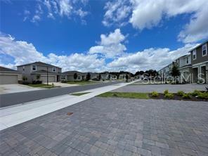 A paved driveway leads to a street lined with modern suburban townhouses under a blue sky — 1309 AXEL GRAESON AVENUE, KISSIMMEE, FL