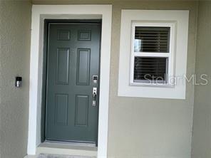 A dark green front door sits next to a window with white trim — 1309 AXEL GRAESON AVENUE, KISSIMMEE, FL