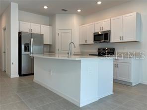 A modern kitchen features white cabinets, stainless steel appliances, and a large central island — 1309 AXEL GRAESON AVENUE, KISSIMMEE, FL