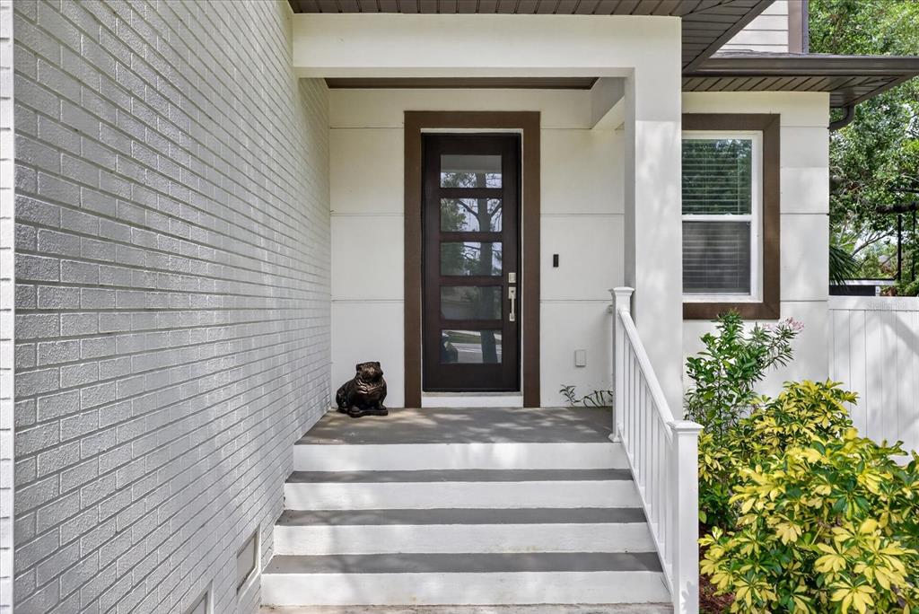 A front porch with white brick walls, a dark wood door, and concrete steps — 4102 S TRASK STREET, TAMPA, FL