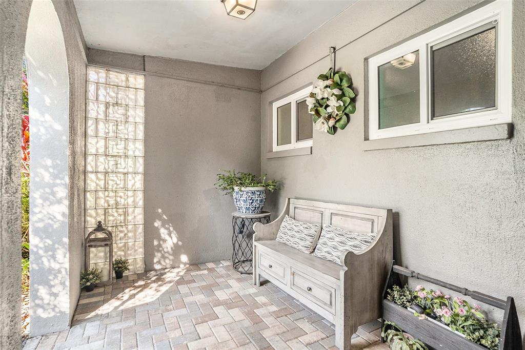 A covered patio features a brick floor, a wooden bench, and a glass block wall — 2134 SERPENTINE CIRCLE S, ST PETERSBURG, FL