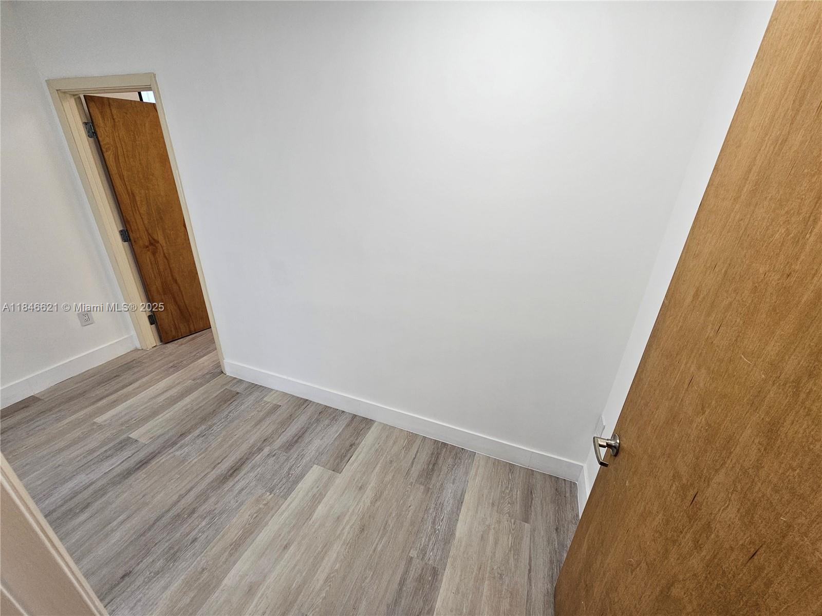 An empty room features white walls, wood-look laminate flooring, and two wooden doors — 12550 Biscayne Blvd # 11, North Miami FL 33181, NORTH MIAMI, FL