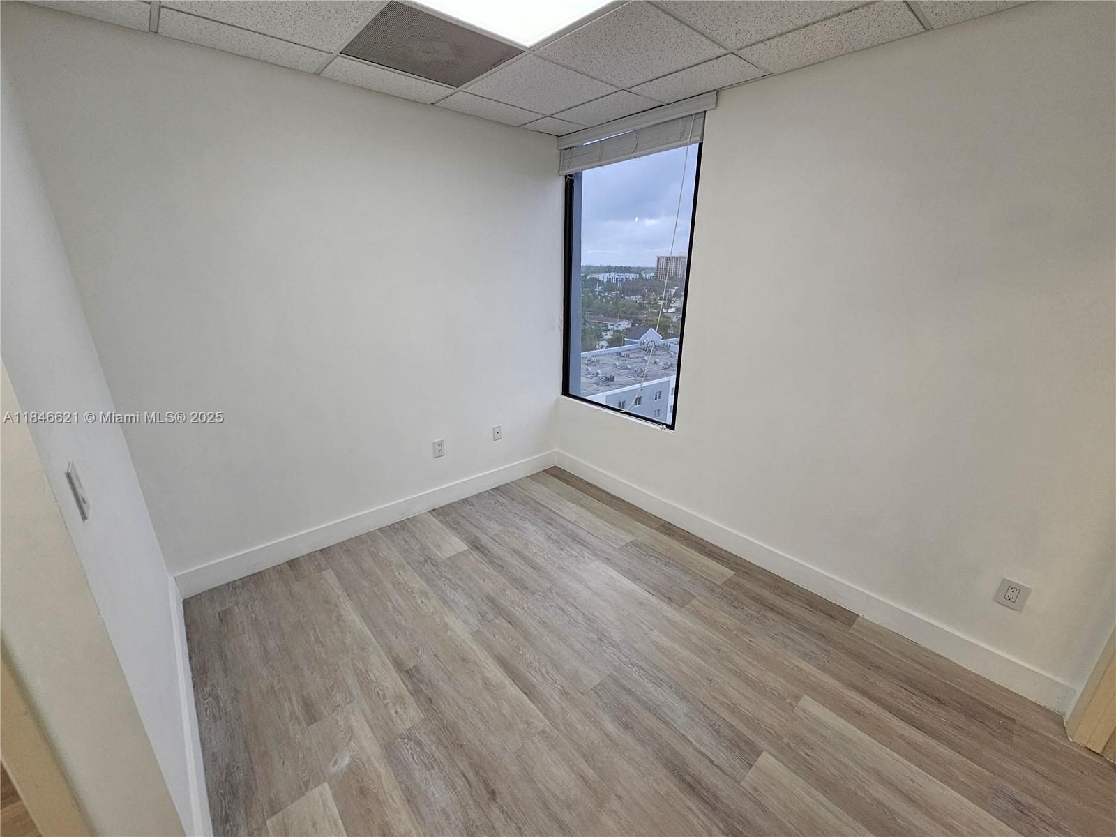 An empty office with white walls, wood-look flooring, and a window overlooking a city — 12550 Biscayne Blvd # 11, North Miami FL 33181, NORTH MIAMI, FL