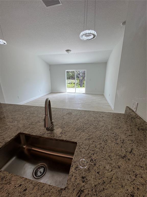 A kitchen sink with a granite countertop overlooks an open living area with sliding doors — 3148 N COVINGTON DRIVE, DELTONA, FL