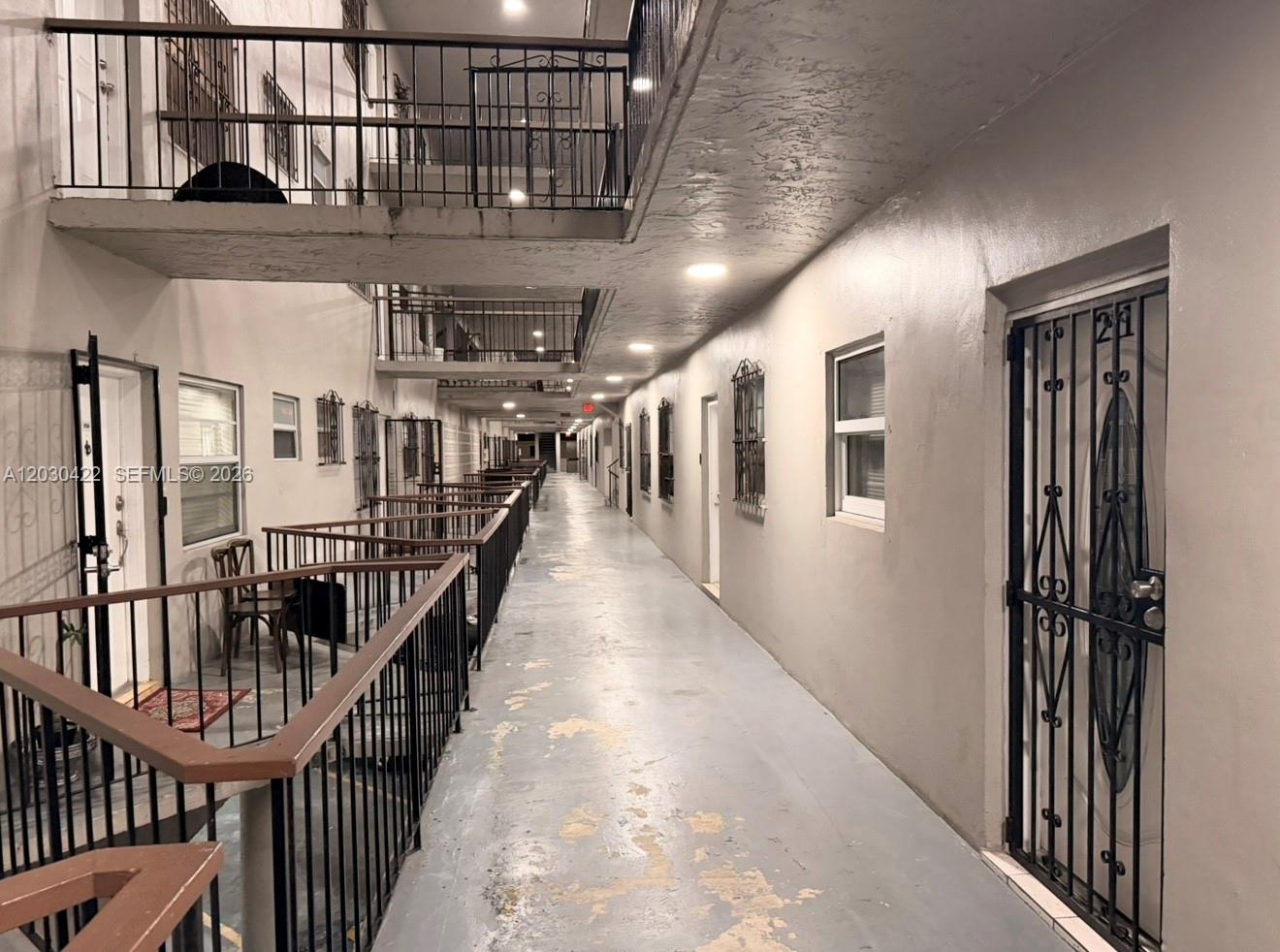 An outdoor apartment building walkway features a concrete floor, metal railings, and security screen doors — 1035 W 77th St # 211, Hialeah FL 33014, HIALEAH, FL