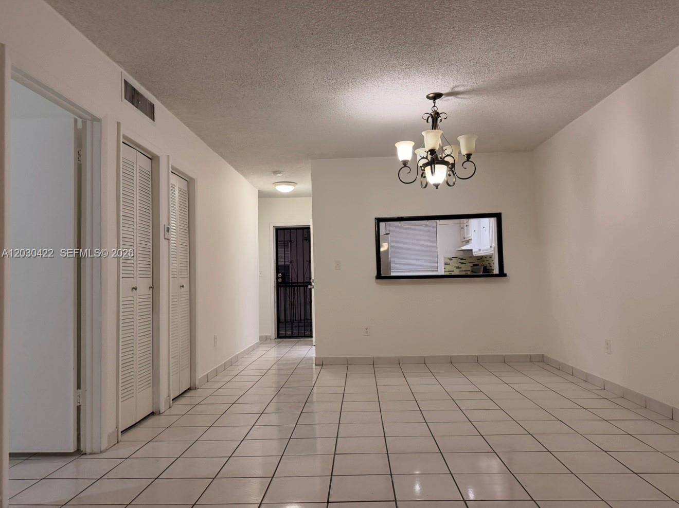 A dining area features white tile flooring, a chandelier, and a pass-through window to the kitchen — 1035 W 77th St # 211, Hialeah FL 33014, HIALEAH, FL