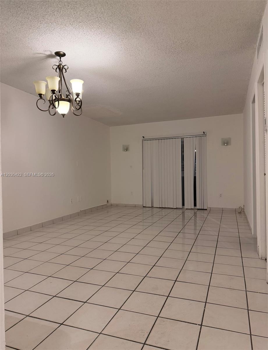 An empty room features white tiled floors, a chandelier, and sliding glass balcony doors — 1035 W 77th St # 211, Hialeah FL 33014, HIALEAH, FL