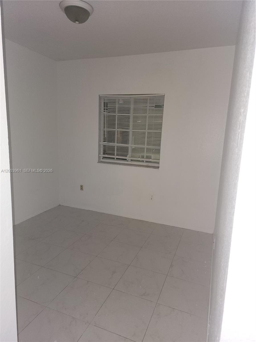 An empty room features white walls, a single window with blinds, and light-colored tile flooring — 6972 NW 179th St # 4, Hialeah FL 33015, HIALEAH, FL
