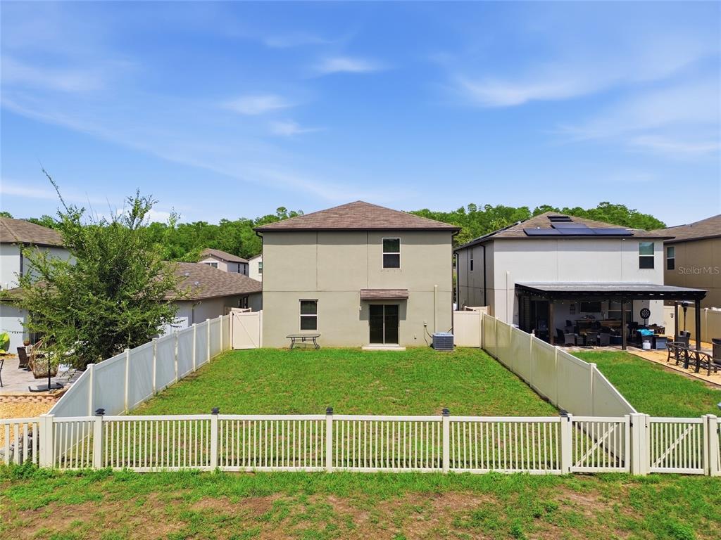 A rear view of a two-story house with a fenced backyard and green lawn — 13393 MARBLE SANDS COURT E, HUDSON, FL