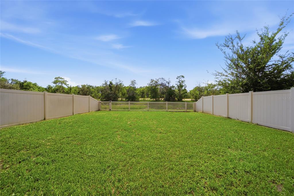 A grassy backyard enclosed by white vinyl fencing with a gate at the rear — 13393 MARBLE SANDS COURT E, HUDSON, FL