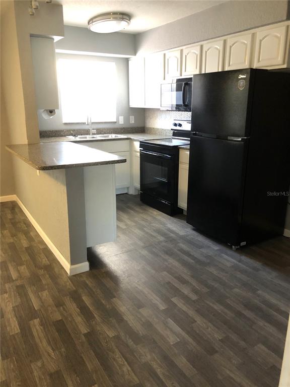 A kitchen features white cabinets, black appliances, a breakfast bar, and wood-look flooring — 9030 BLIND PASS ROAD UNIT C10, ST PETERSBURG, FL