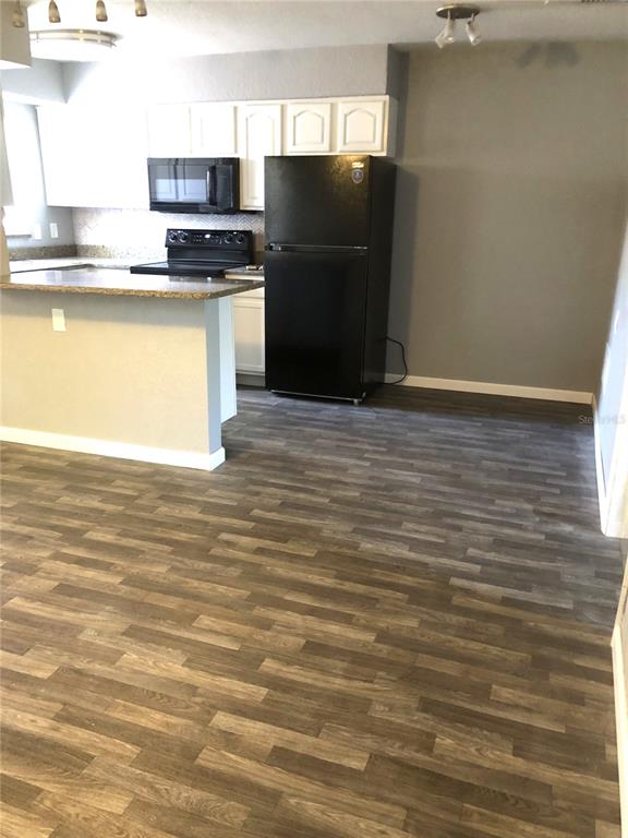 A kitchen features white cabinets, black appliances, a granite-topped breakfast bar, and wood-look flooring — 9030 BLIND PASS ROAD UNIT C10, ST PETERSBURG, FL