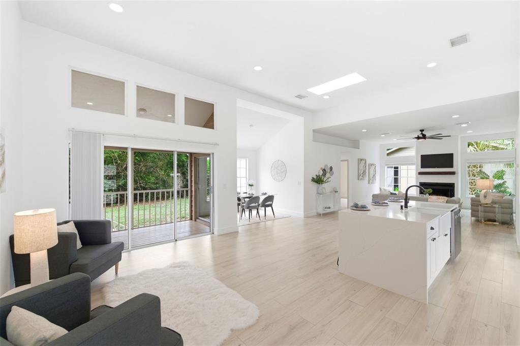 An open-concept living area with a kitchen island, light wood floors, and sliding glass doors — 4401 LITTLE JOHN TRAIL, SARASOTA, FL
