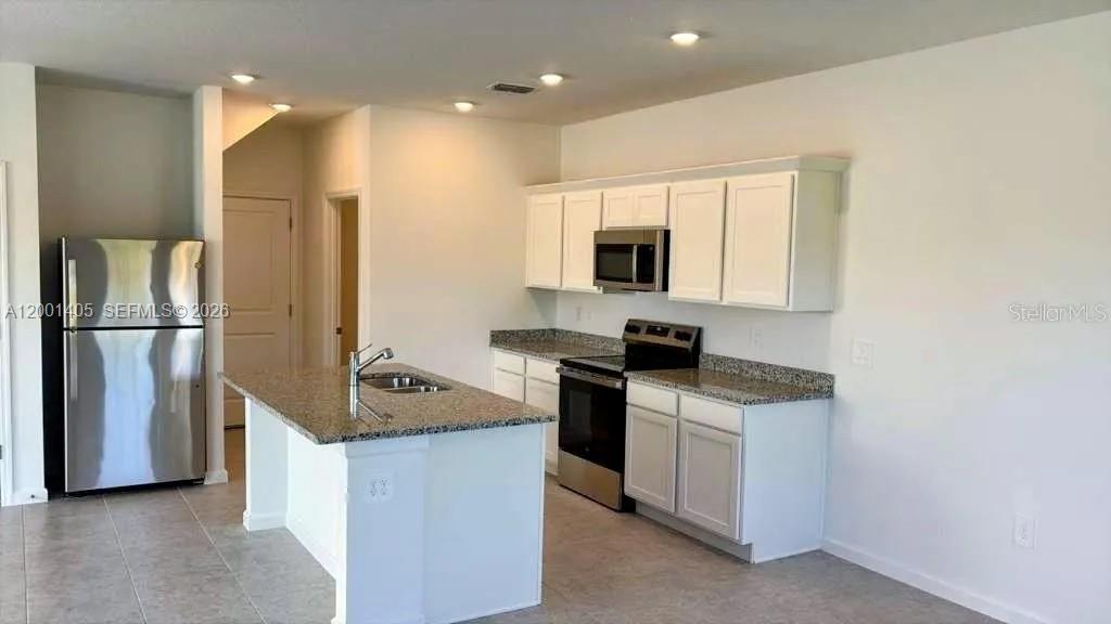 A kitchen features white cabinets, granite countertops, stainless steel appliances, and a central island — KISSIMMEE, FL
