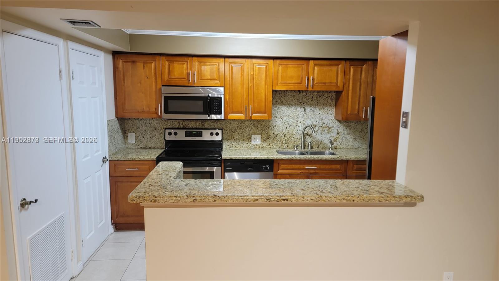 A kitchen features wood cabinets, granite countertops, and stainless steel appliances behind a breakfast bar — 8401 SW 107th Ave # 234E, Miami FL 33173, MIAMI, FL