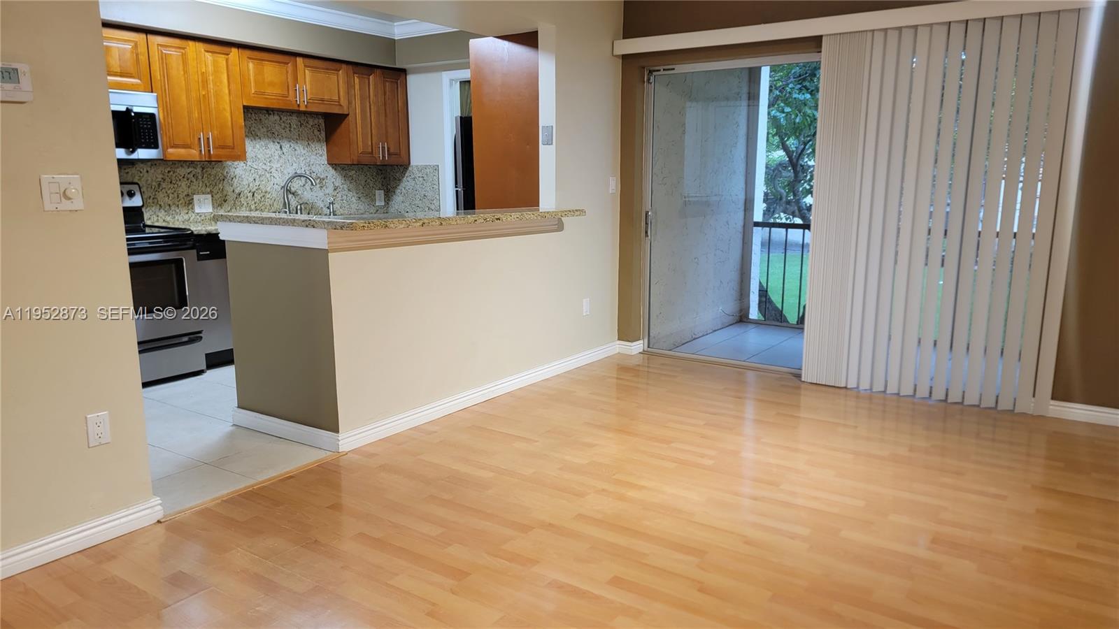 A kitchen with wood cabinets and granite counters opens to a living area with balcony — 8401 SW 107th Ave # 234E, Miami FL 33173, MIAMI, FL