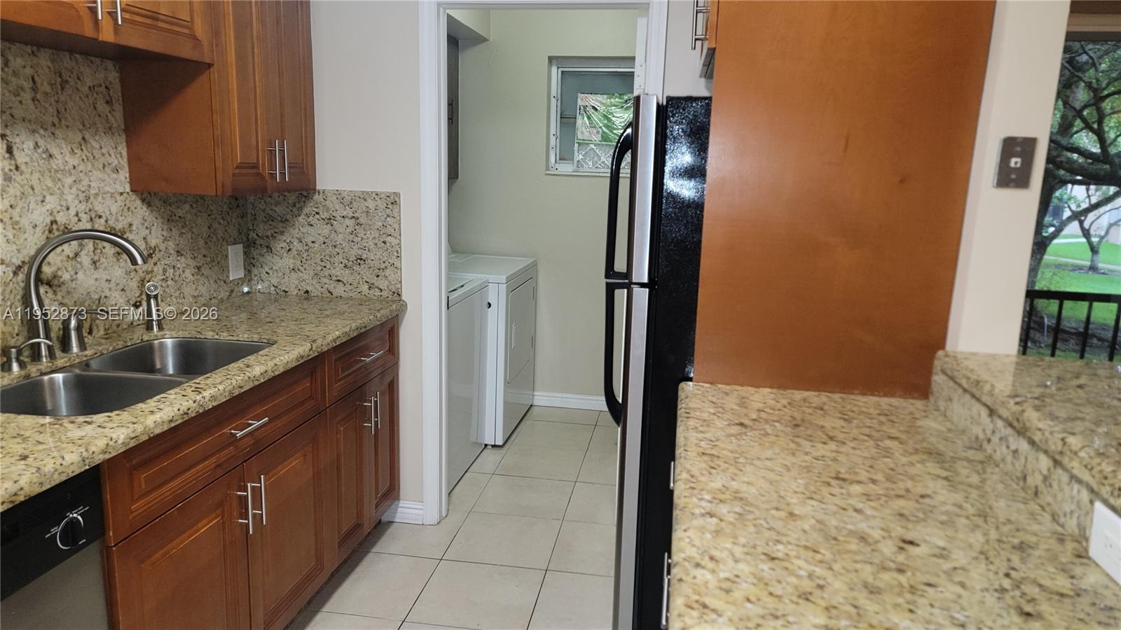 A kitchen with wood cabinets, granite countertops, and an adjacent laundry room with appliances — 8401 SW 107th Ave # 234E, Miami FL 33173, MIAMI, FL