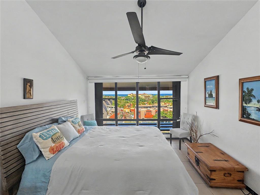 A bedroom with a king bed, ceiling fan, and a large window overlooking the ocean — 170 Palmas Dr, Humaca 170 PALMAS DR UNIT B7, HUMACAO, PR