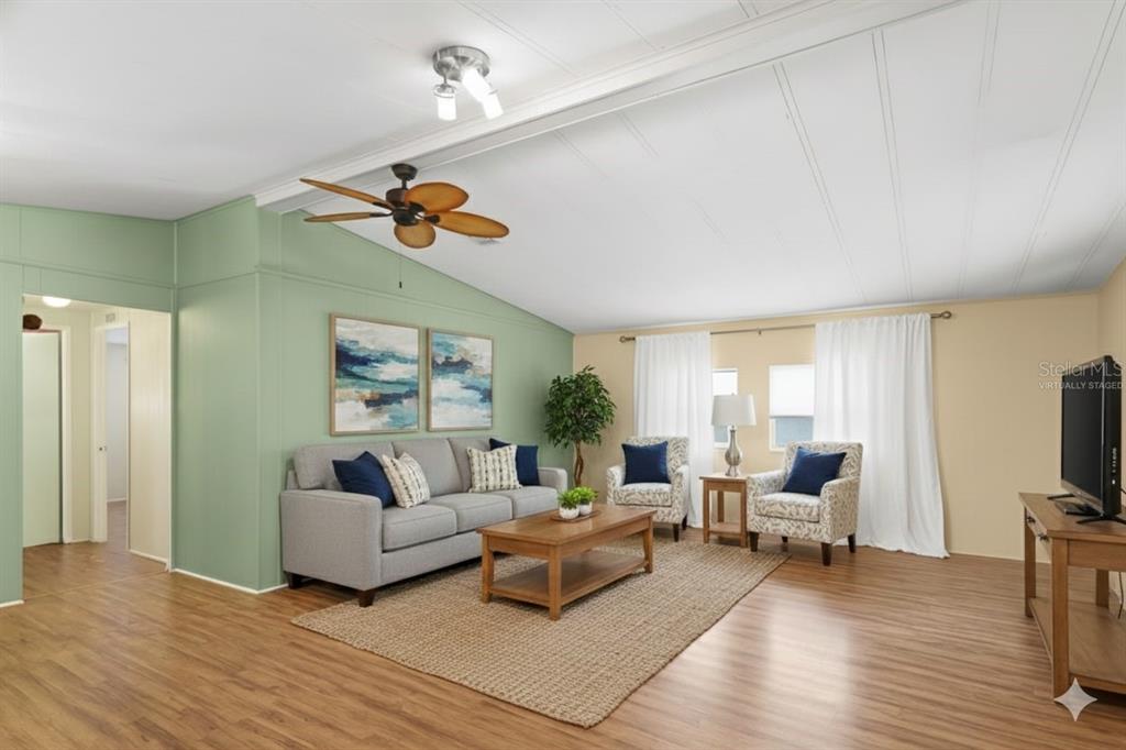 This open-concept living room and kitchen features green walls, white cabinets, and wood-look flooring — 154 RAROTONGA ROAD, NORTH PORT, FL