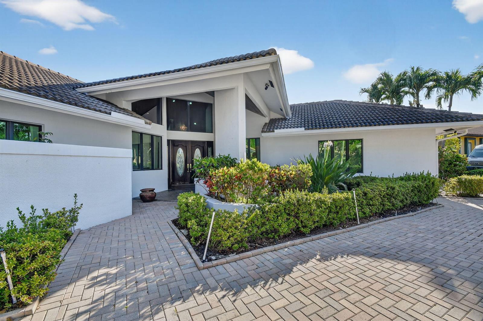A white house with a dark tile roof features a paved driveway and front walkway — 2410 Embassy Drive, West Palm Beach FL 33401, WEST PALM BEACH, FL