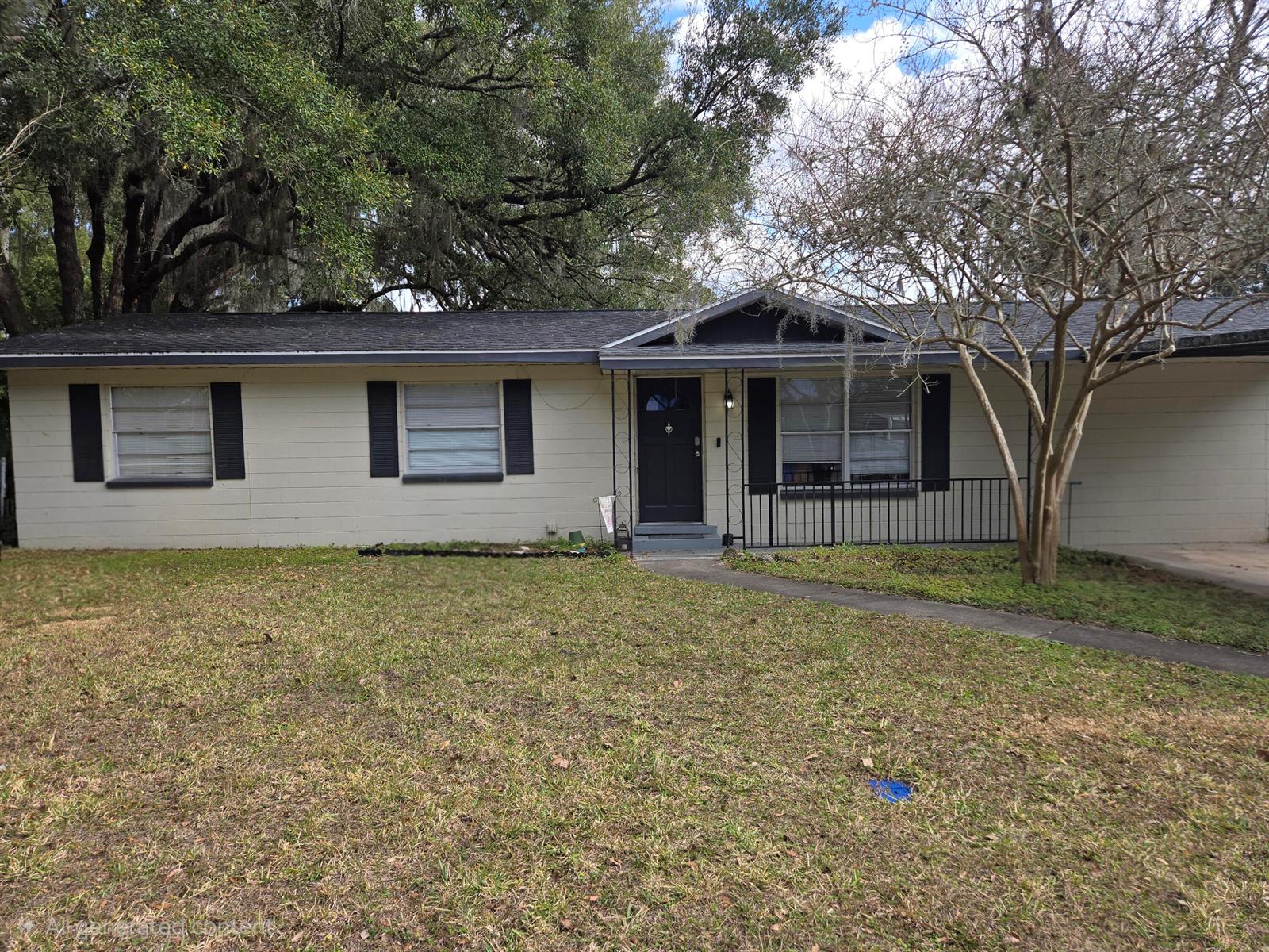 A single-story house with beige siding, black shutters, and a dark front door — 211 NE 3rd Terrace, Williston FL 32696, WILLISTON, FL