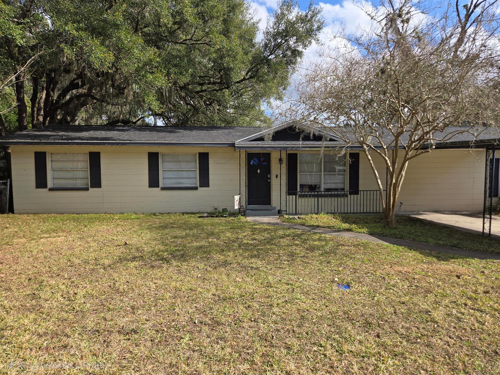 A single-story house with light siding, black shutters, and a dark roof under trees — 211 NE 3rd Terrace, Williston FL 32696, WILLISTON, FL