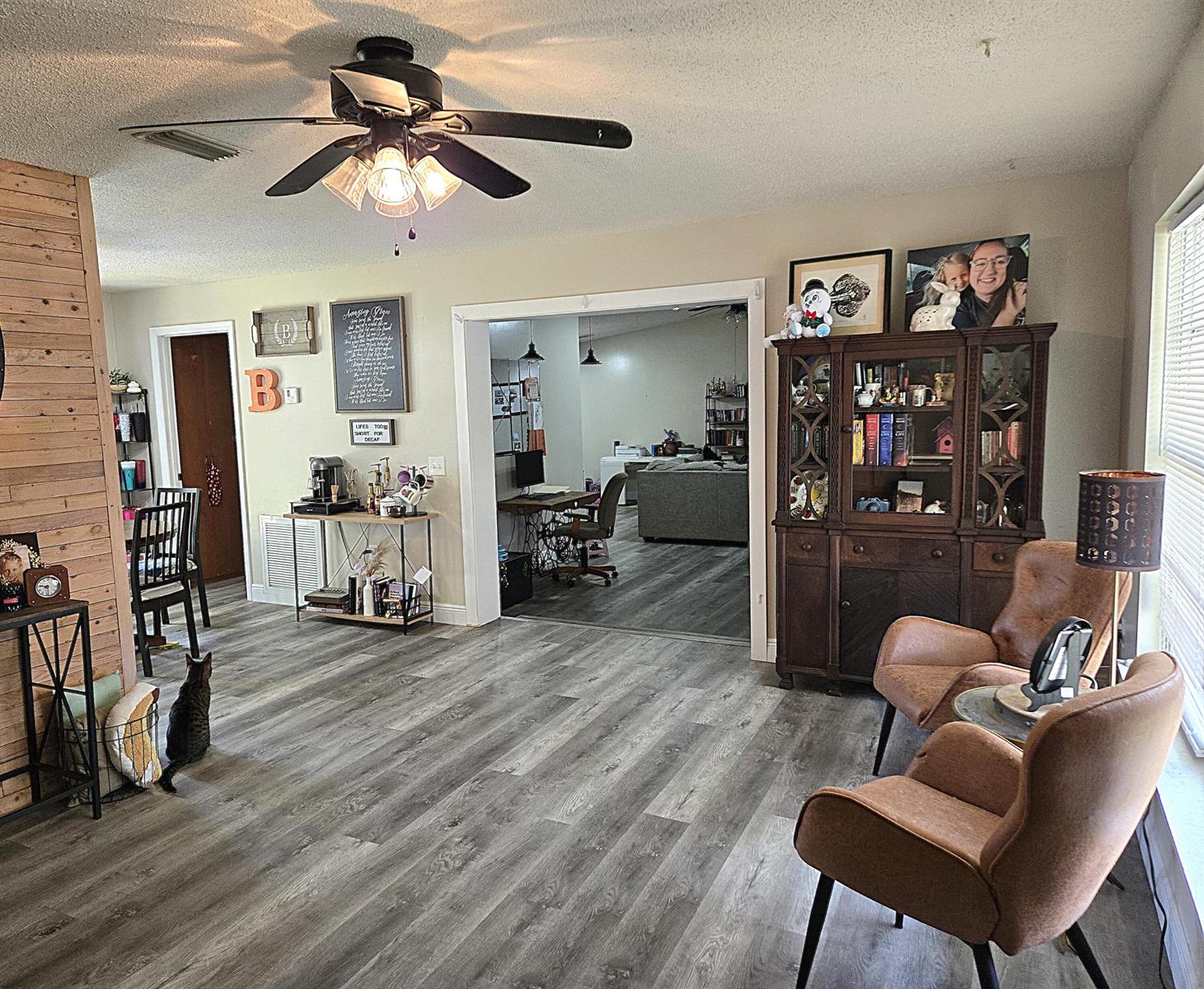 A living area with wood-look flooring, a ceiling fan, a hutch, and two brown chairs — 211 NE 3rd Terrace, Williston FL 32696, WILLISTON, FL