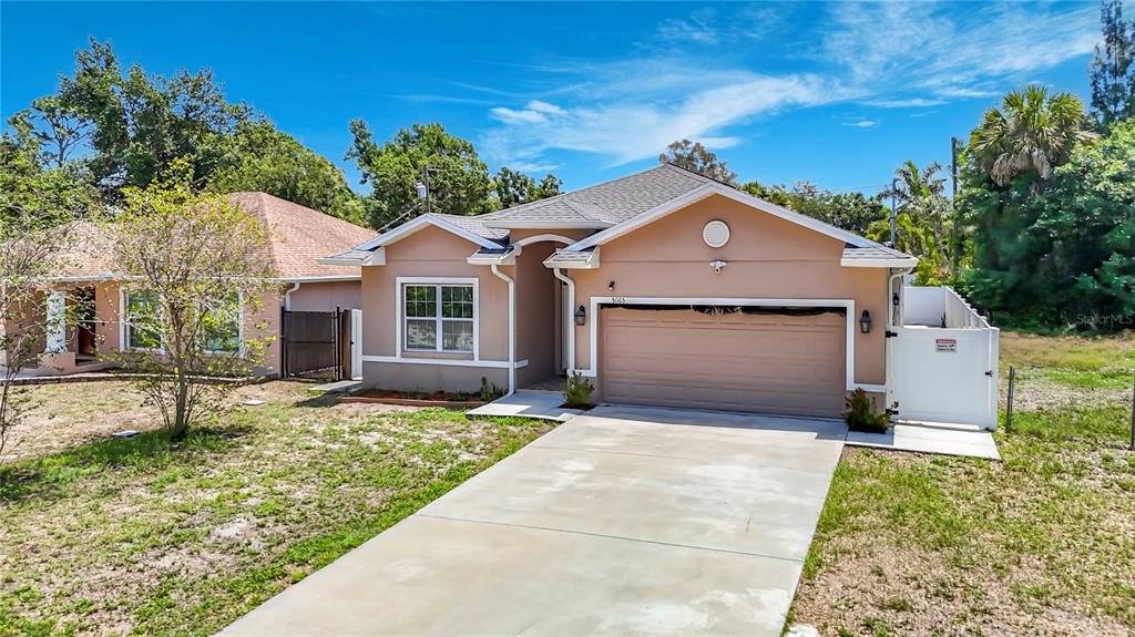 A tan, single-story house with a concrete driveway, a two-car garage, and a white fence — 5065 67TH WAY N, ST PETERSBURG, FL