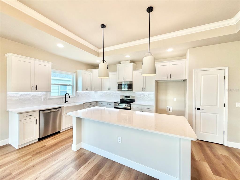 A modern kitchen features white cabinetry, a large center island, and stainless steel appliances — 146 SW 212TH DRIVE, NEWBERRY, FL