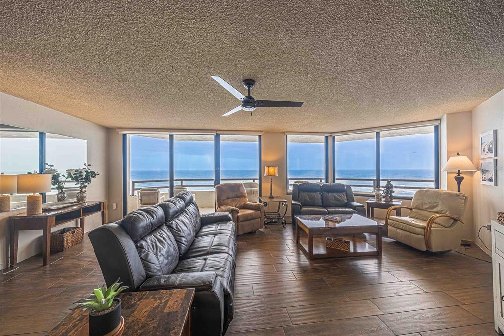A living room with tile floors, leather furniture, and floor-to-ceiling windows overlooking the ocean — 3855 S ATLANTIC AVENUE UNIT 1004, DAYTONA BEACH, FL