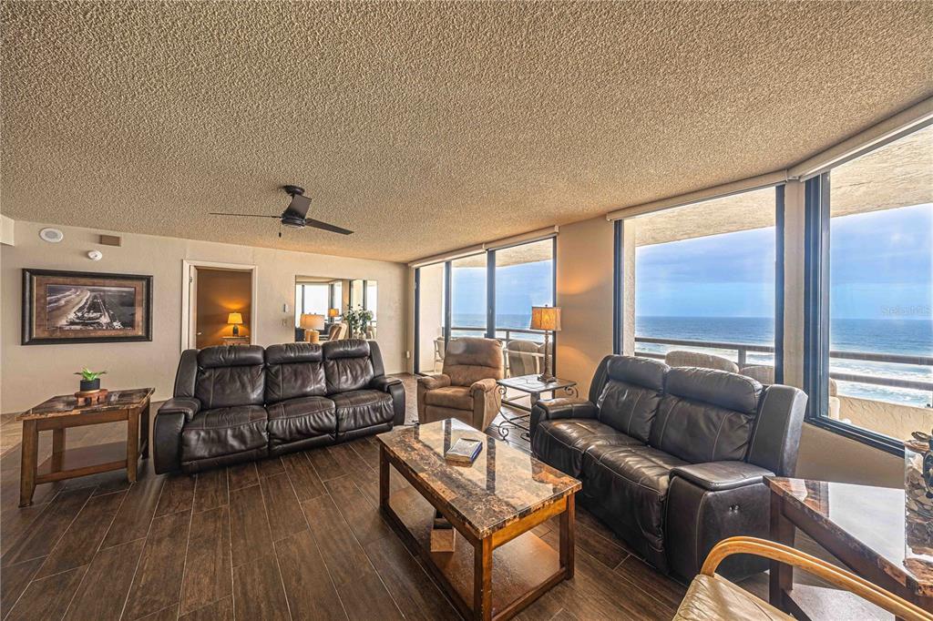 A living room with dark leather furniture, tile floors, and large windows overlooking the ocean — 3855 S ATLANTIC AVENUE UNIT 1004, DAYTONA BEACH, FL