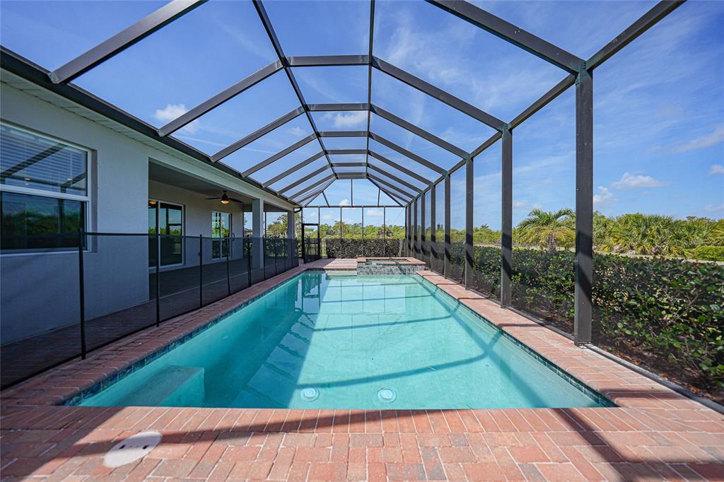 A rectangular swimming pool with a spa is enclosed by a screened lanai and brick pavers — 14332 PONCE DE LEON TRAIL, PORT CHARLOTTE, FL