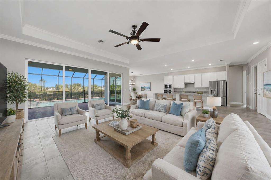 A bright, open-concept living room and kitchen area features neutral furniture, tile floors, and sliding glass doors — 14332 PONCE DE LEON TRAIL, PORT CHARLOTTE, FL
