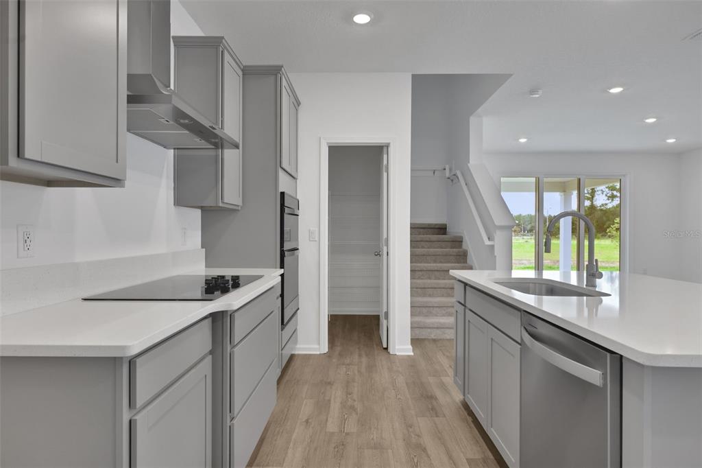 A modern kitchen features gray cabinets, white countertops, stainless steel appliances, and a staircase nearby — 3890 HOLSTEIN WAY, GREEN COVE SPRINGS, FL