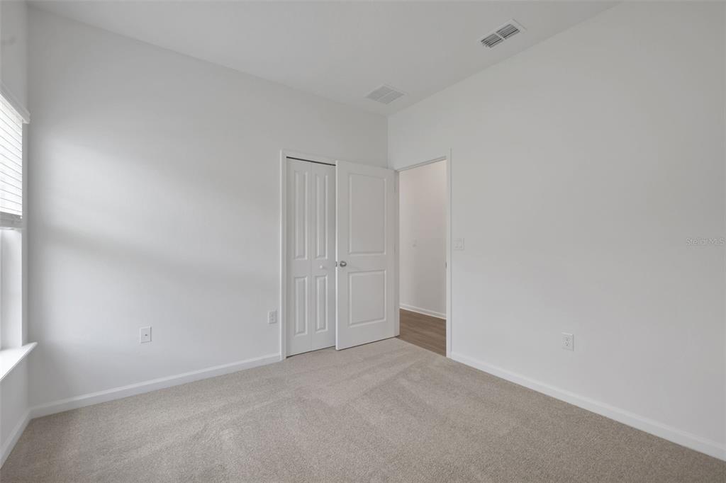 A bedroom features white walls, beige carpeting, a closet with double doors, and an open doorway — 3890 HOLSTEIN WAY, GREEN COVE SPRINGS, FL