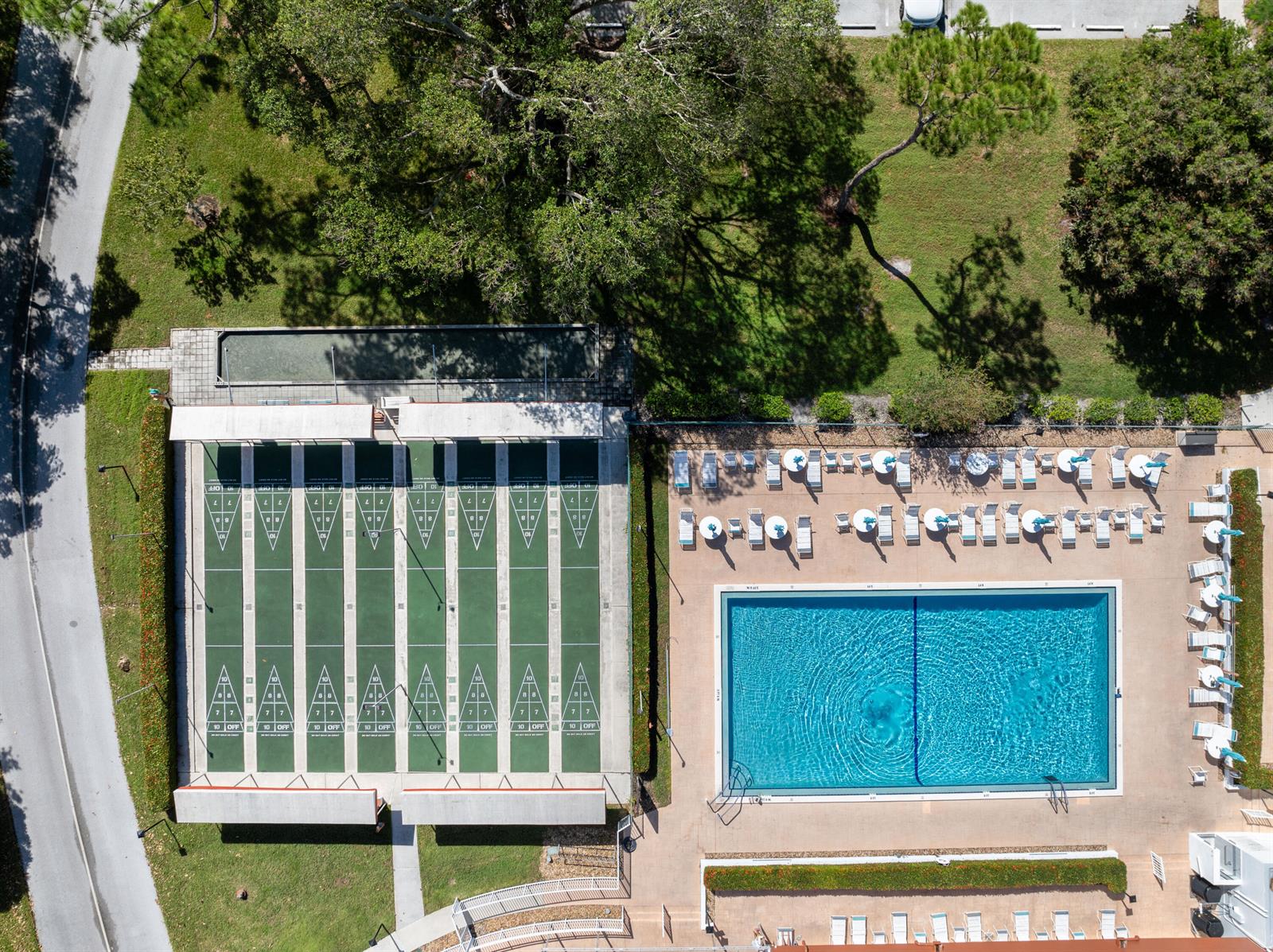 An aerial view shows a swimming pool and shuffleboard courts surrounded by grass and trees — 2600 SE Ocean Boulevard # N14, Stuart FL 34996, STUART, FL