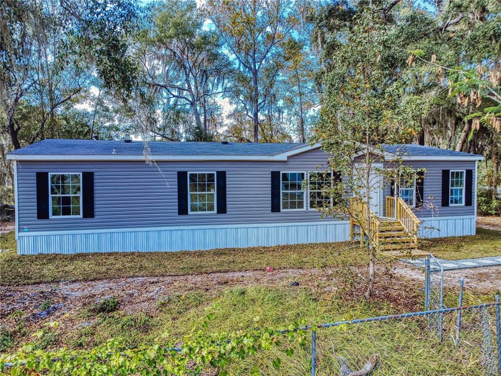 A gray manufactured home with white skirting and wooden stairs sits in a wooded lot — 4300 NE 175TH STREET ROAD, CITRA, FL