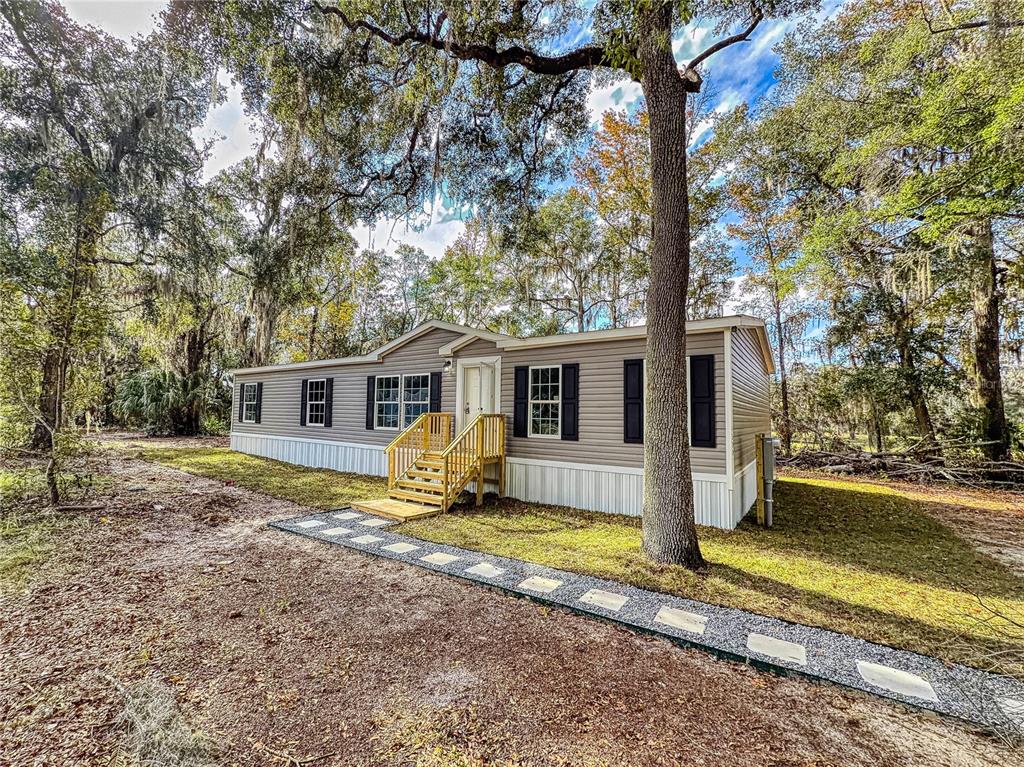 A tan manufactured home with black shutters sits in a wooded lot with a walkway — 4300 NE 175TH STREET ROAD, CITRA, FL
