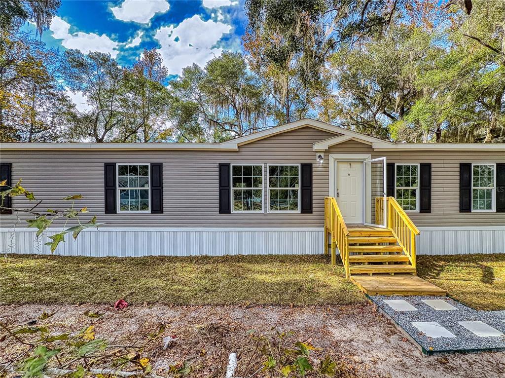 A tan manufactured home with black shutters and wooden steps leading to the front door — 4300 NE 175TH STREET ROAD, CITRA, FL