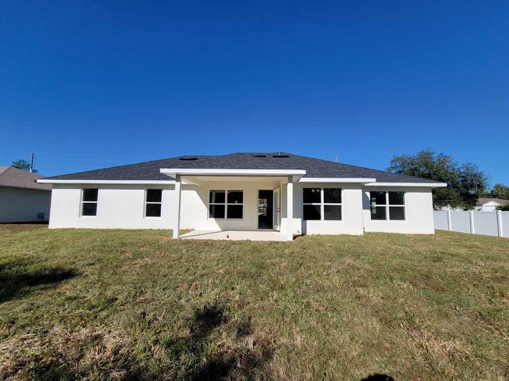 The rear exterior of a white single-story house features a covered patio and lawn — 14590 SW 69TH COURT ROAD, OCALA, FL
