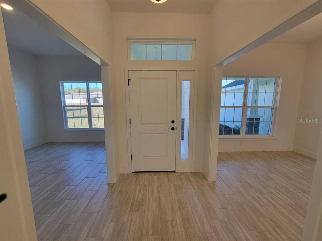 An entryway with light wood-look tile flooring, a white front door, and two adjacent rooms — 14590 SW 69TH COURT ROAD, OCALA, FL
