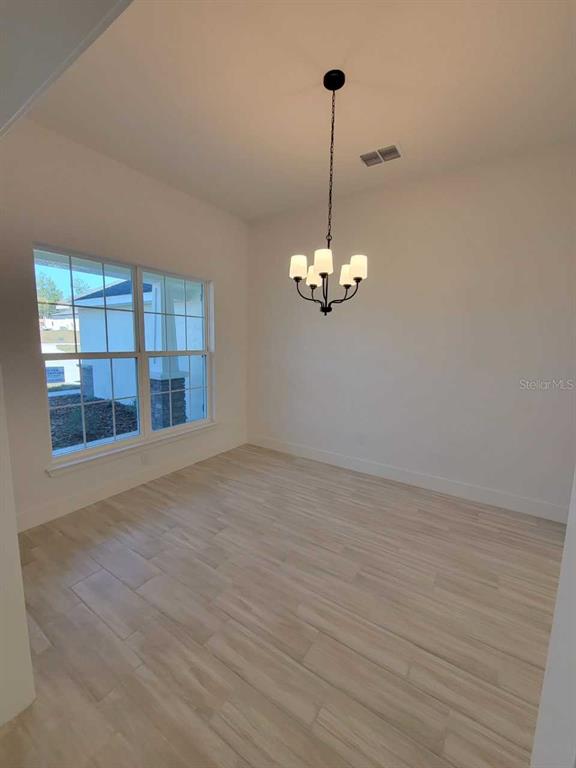A dining room with light wood-look tile flooring, white walls, and a five-light chandelier — 14590 SW 69TH COURT ROAD, OCALA, FL