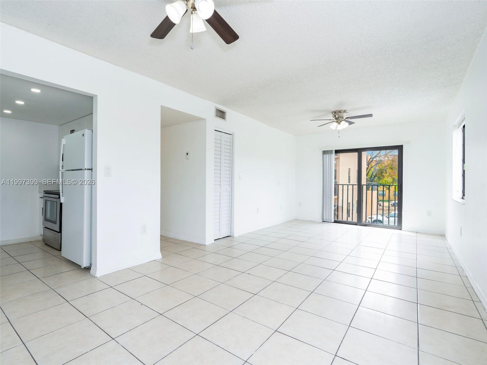 An open-concept living area features white walls, tile flooring, two ceiling fans, and a kitchen — 1490 W 42nd Pl # 206, Hialeah FL 33012, HIALEAH, FL