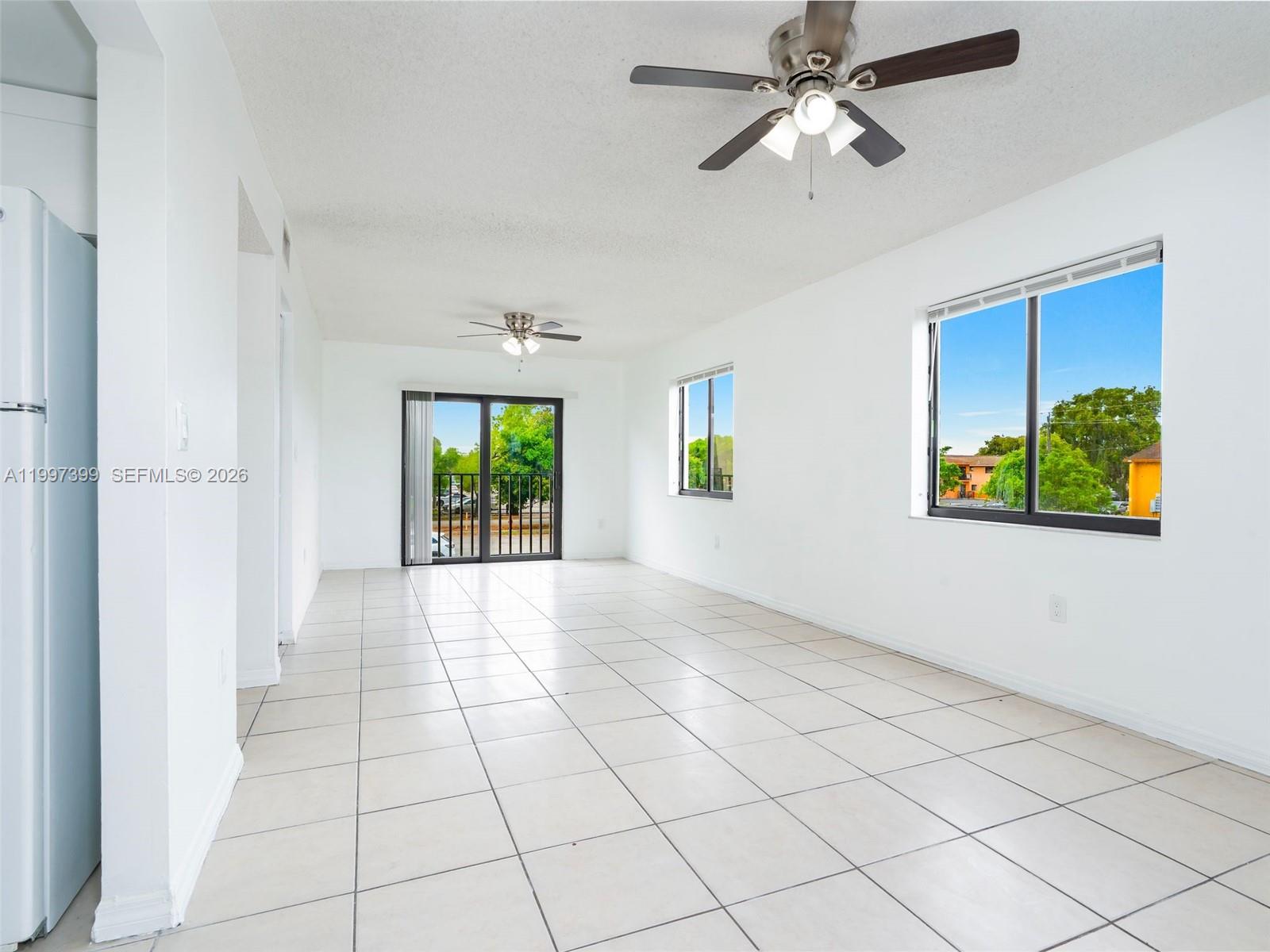 An empty room features white walls, light-colored tile flooring, two ceiling fans, and large windows — 1490 W 42nd Pl # 206, Hialeah FL 33012, HIALEAH, FL