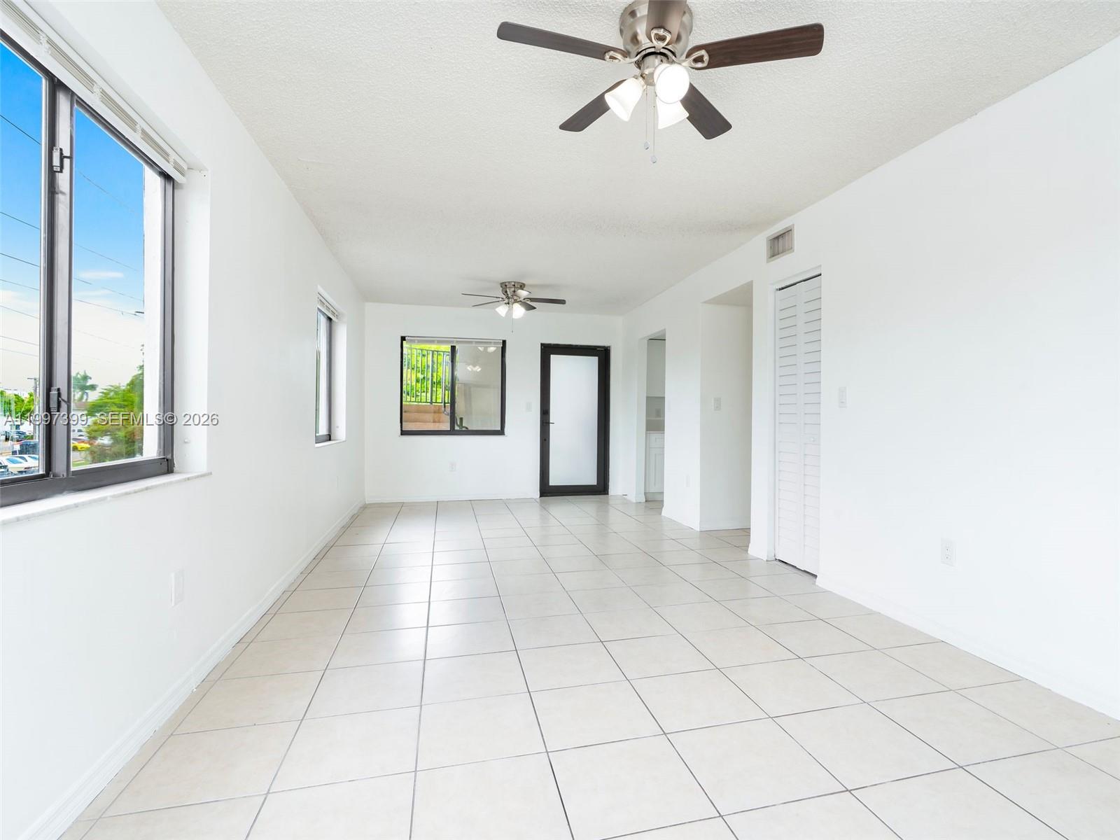 A bright, empty room features white walls, tiled flooring, two ceiling fans, and several windows — 1490 W 42nd Pl # 206, Hialeah FL 33012, HIALEAH, FL