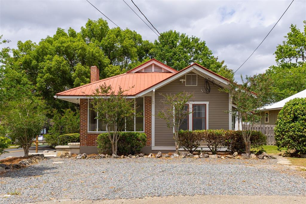 A single-story house with a red metal roof, brick accents, and a gravel driveway — 825 SE SANCHEZ AVENUE, OCALA, FL