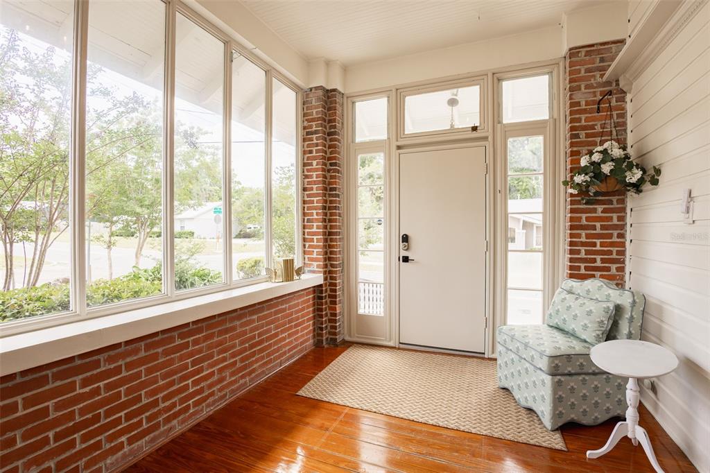 A sunroom with brick walls, large windows, a white door, and hardwood flooring — 825 SE SANCHEZ AVENUE, OCALA, FL