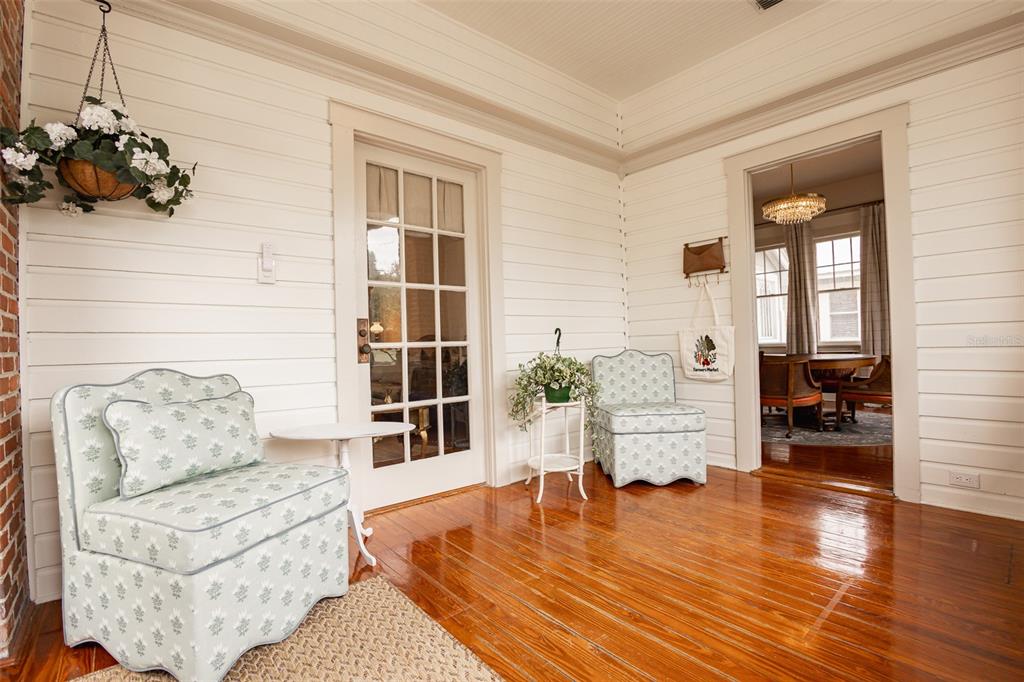 A sunroom with white shiplap walls, hardwood floors, two patterned chairs, and a glass door — 825 SE SANCHEZ AVENUE, OCALA, FL